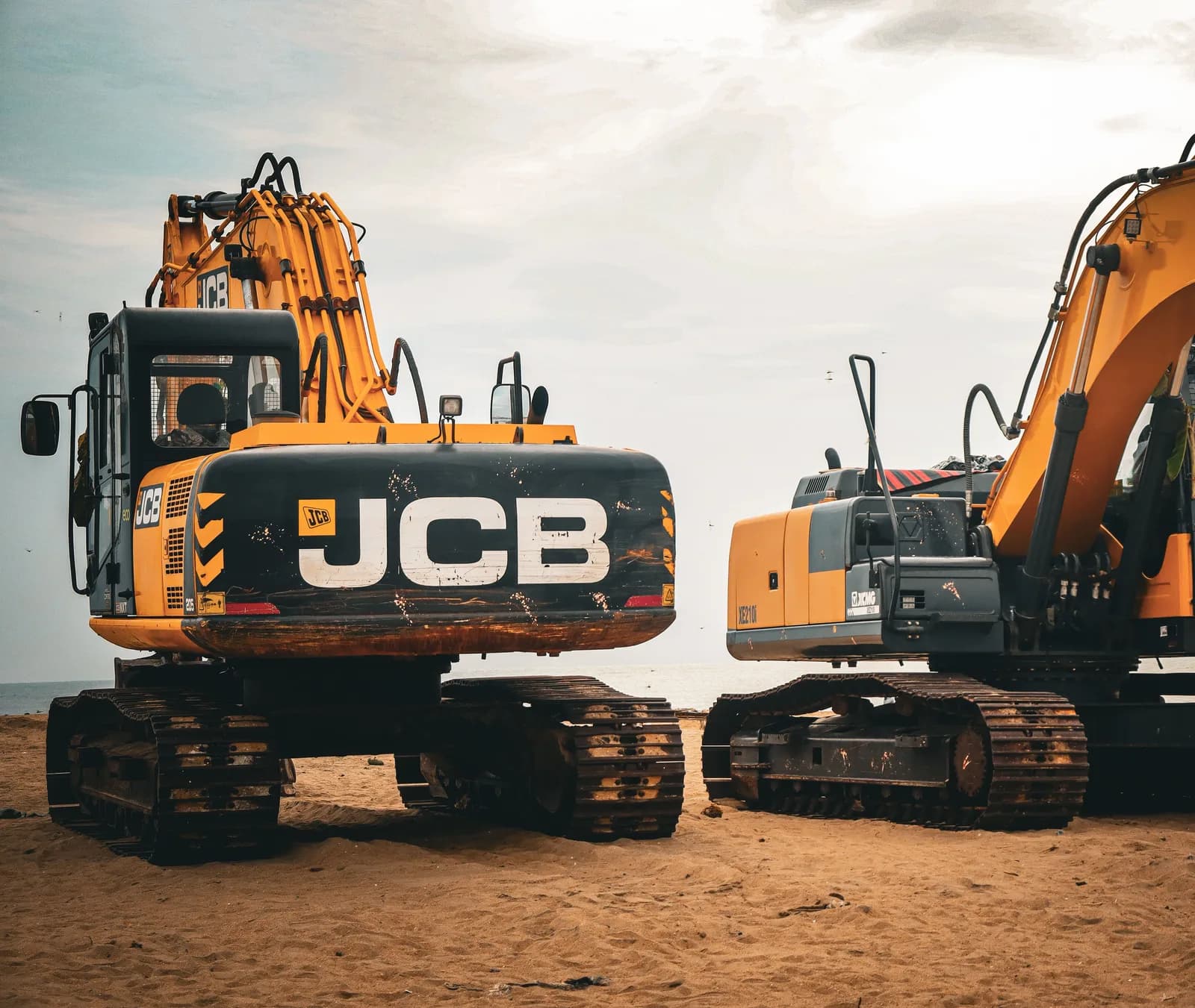Two tracked JCB excavators parked side by side on a sandy site